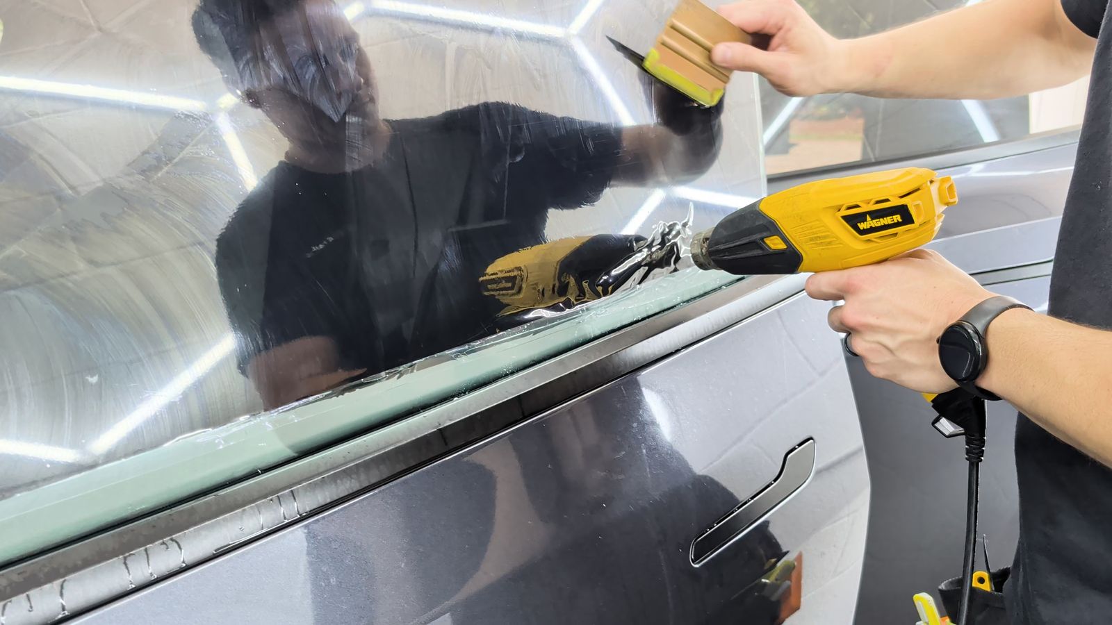 Heat gun and squeegee setting ceramic film on a door window at Taggart Films, installer reflected in the glass